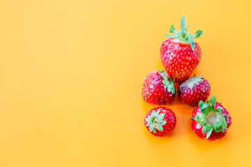 Five fresh red strawberries with green stems are arranged on a vibrant orange background. This...