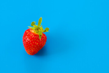 A fresh red strawberry with a green stem lies on a vibrant blue background, creating a striking color contrast. This juicy berry is ideal for culinary and summer themes.