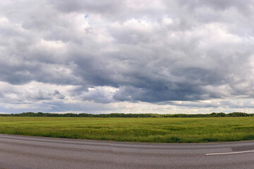 Huge green field under cloudy sky next to winding road in rural landscape