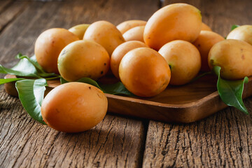 Fresh Ripe Yellow Mangoes with Green Leaves on Wooden Table in Natural Light