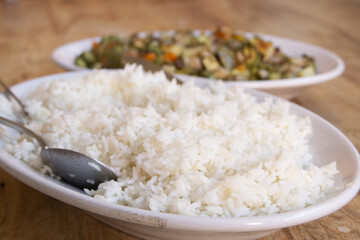 serving spoons resting on fluffy white rice next to cooked vegetables