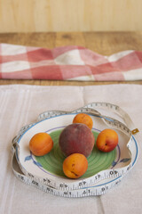Measuring tape wrapped around plate holding peach and apricots symbolizing healthy diet