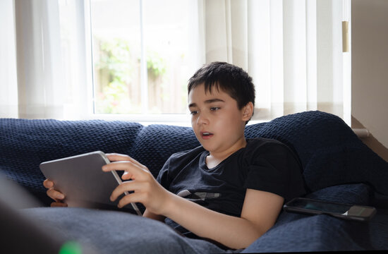 Kid Online Education,Asian Child using tablet computer Ai technology for homework,Schoolboy watching online movie, playing virtual game sitting on sofa,Concept Kid and digital technology addiction