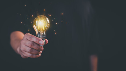 Young man holding a glowing light bulb in a dark background, symbolizing creativity, creative solutions, innovation, and bright ideas. Business global internet connection application technology.