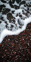 Close-up of dark pebbles on a beach with white sea foam washing over them.