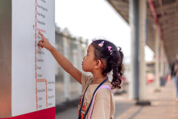 A little Asian girl looks at a train map at a station in Jakarta for her journey