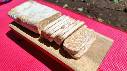 Sliced raw tempeh on cutting wooden board. Traditional Indonesian food made from fermented soy bean.