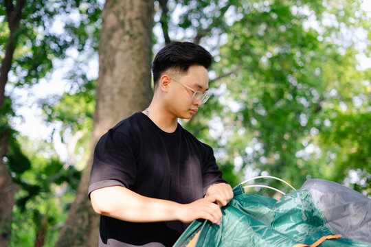 Young man sets up tent in a lush green park on a sunny day for an outdoor camping experience with friends