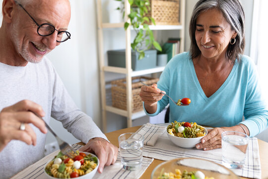 Mature married couple eating meal together at home dining table.