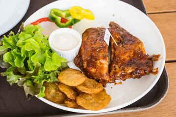 Close-up of grilled ribs with barbecue sauce served with potato slices, dip, and fresh salad on a white plate