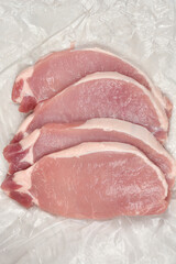Four raw pork chops arranged on a wrinkled white surface.