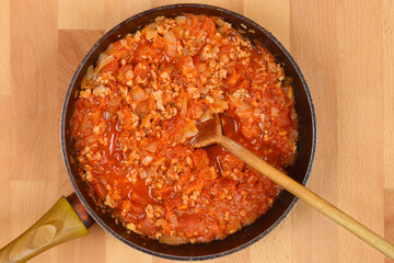 A ground meat, onion, and tomato sauce in a pan with a wooden spoon, photographed from a top-down angle