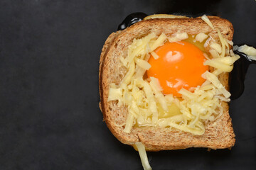 Toast with cut-out centers, filled with raw eggs and grated cheese, on a dark baking sheet