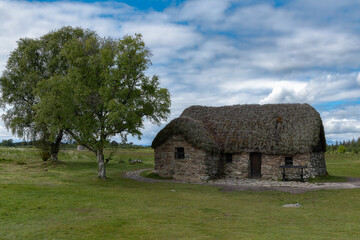Obraz premium A traditional Highlander stone cottage with a thatched roof, located on the historic Culloden Battlefield near Inverness, Scotland.