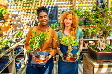 Two young women holding bonsai trees in plant nursery