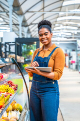 Smiling african american saleswoman using digital tablet in supermarket fruit section