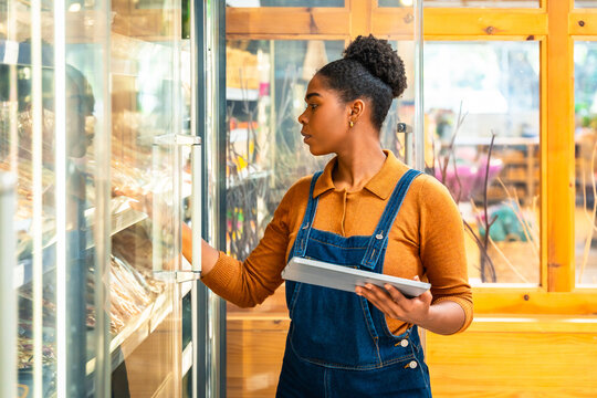 Saleswoman checking food supplies using digital tablet in store refrigerator