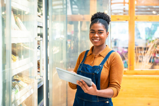 Smiling saleswoman using digital tablet checking stock in refrigerated section of supermarket - Powered by Adobe