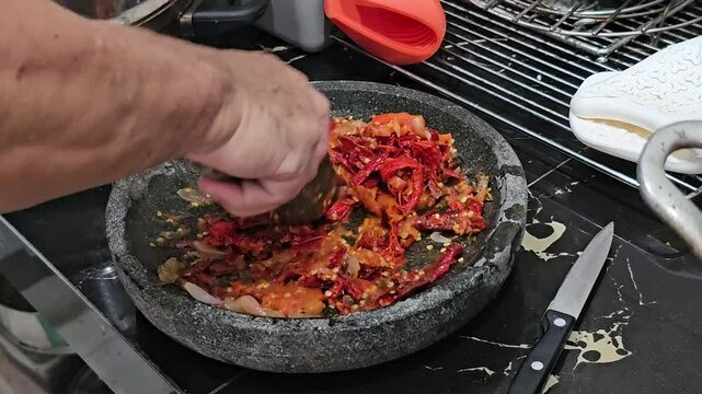 cooking in the kitchen,red hot chili pepper,A man making sambal uleg or sambal ulek,homemade Indonesian traditional chili paste in a traditional molcajet or stone mortar and pestle.Handmade sambal