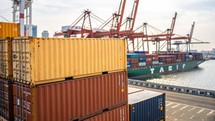 Fototapeta premium Import tariff policy concept. Cargo containers stacked at a harbor with ships in the background.