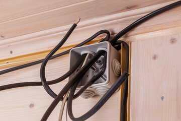 Open junction box with exposed cables against wooden wall highlights electrical installation process before connection and insulation.