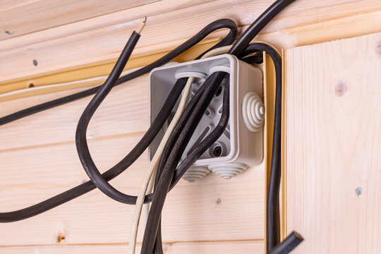 Open electrical junction box with multiple black and white wires protruding in wooden wall, showing installation stage and safety importance.