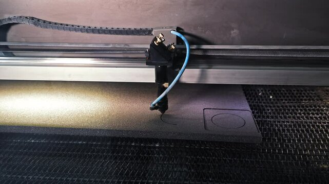 Laser cutting machine engraving foam material. Close-up of an industrial laser cutter precisely engraving shapes into a sheet of foam.