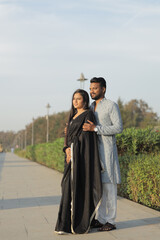 An affectionate Indian couple dressed in elegant traditional clothing shares a tender moment outdoors on a sunlit pathway