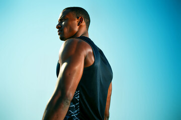 A dedicated athlete stands confidently against a vibrant blue sky, showcasing strength and determination during an outdoor training session. Generative AI.