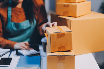 Fototapeta premium Startup SME small business entrepreneur of freelance Asian woman wearing apron using laptop and box to receive and review orders online to prepare to pack sell to customers, online sme business ideas.