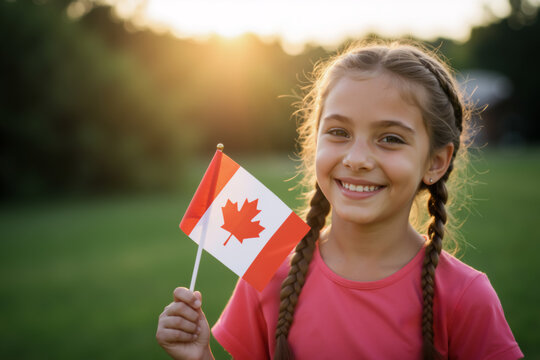 Close up portrait of smiling girl with braided pigtails holding Canadian flag outdoors at sunset. Child celebrating Canada Day.