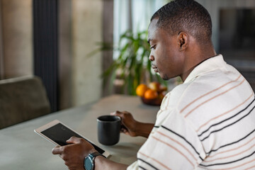 Smiling handsome african man using tablet with social networks at home, happy freelancer making online shopping