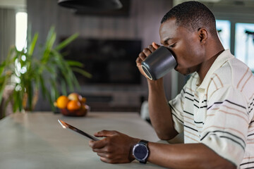 Smiling handsome african man using tablet with social networks at home, happy freelancer making online shopping