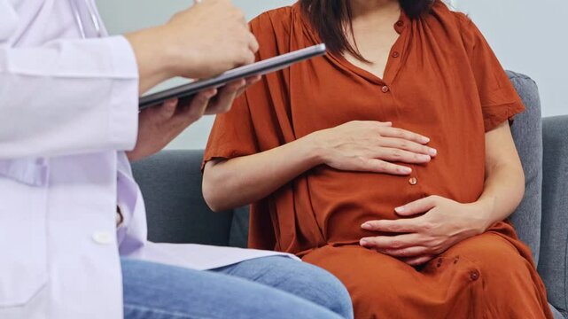 Male obstetrician gynecologist, maternal-fetal medicine specialist examines the health pregnant woman and her nine-month fetus. Sitting and taking notes with interest in order to diagnose symptoms.