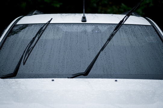 Car windshield with rain drops and frameless wiper blade. Car windshield wiper cleaning water drops from glass while.