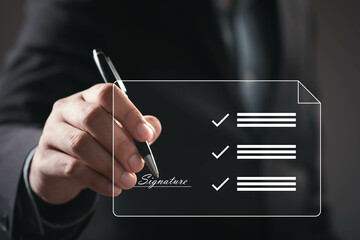 A hand holding a pen is about to sign a document featuring checkmarks, symbolizing approval and...