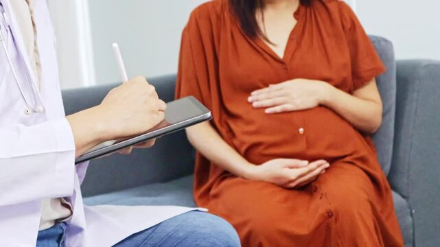 Male obstetrician gynecologist, maternal-fetal medicine specialist examines the health pregnant woman and her nine-month fetus. Sitting and taking notes with interest in order to diagnose symptoms.