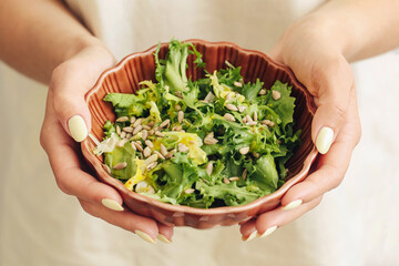 Woman holding green salad bowl. Healthy vegetarian lunch with sprouts and pumpkin seeds. Top view on white background. Fresh and natural clean eating concept. Fitness diet lifestyle.