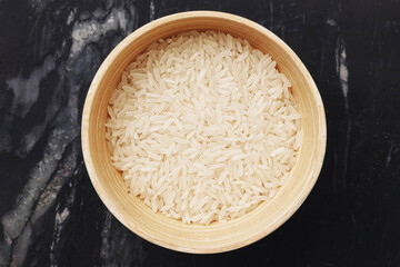 White rice in bamboo bowl. Raw basmati or jasmine grains. Top view on dark marble table. Healthy...