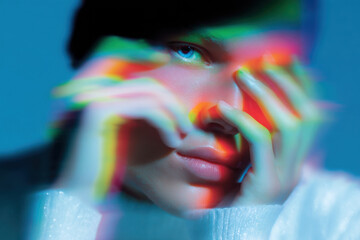 Young person touching face with colorful light projections