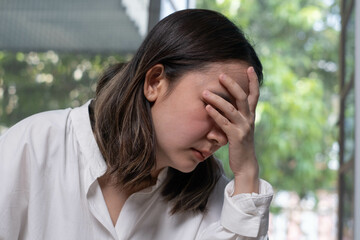 A woman in a white shirt expresses distress, covering her face with her hand, suggesting feelings of stress or anxiety in a serene environment.