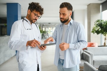 Doctor showing information on tablet to patient in clinic hall