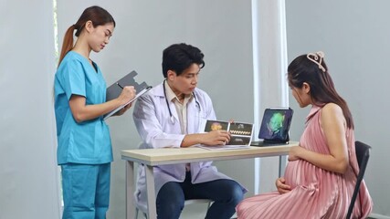 Male obstetrician, gynecologist maternal fetal medicine specialist examines pregnant woman ultrasound results looks at laptop with interest and discusses with female nurse assistant recording results.