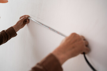 Close-up of elderly builder hands measuring wall with tape measure. Renovation and construction...