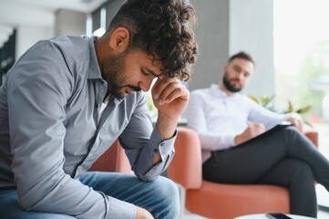 Upset man suffering from ptsd visiting psychologist for therapy session