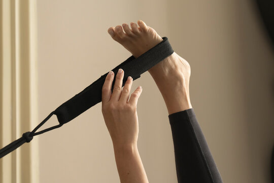 Close-up of woman using a strap for a leg stretching exercise in a yoga or pilates practice.