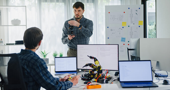 Team adult male engineer develop present AI robotics hand project at tech workspace. Artificial intelligence, collaboration support prototype development, robotic, debugging, machine learn, training.