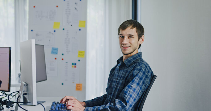 Portrait confident smiling male programmer working with robotics code AI software and looking at camera in tech office. Artificial intelligence dashboard, robotics, user interface, machine learning.