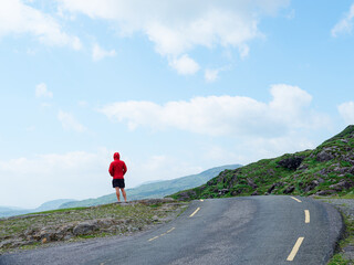A person with a red hooded sweatshirt is standing on a rocky outcrop and looking out towards the scenic views of the Gap of Dunloe in County Kerry, Ireland.