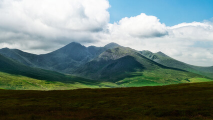 A breathtaking panorama of rolling hills and craggy mountain peaks under a pale sky. Untamed landscape.